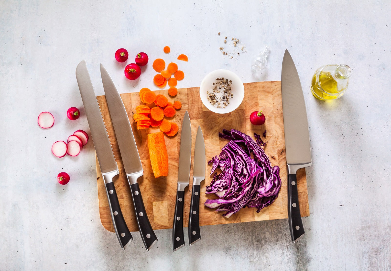 Knives on a wooden cutting board with chopped vegetables on a light gray background